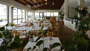 Un comedor amplio con mesas y sillas de madera, ventanas grandes y plantas en macetas.