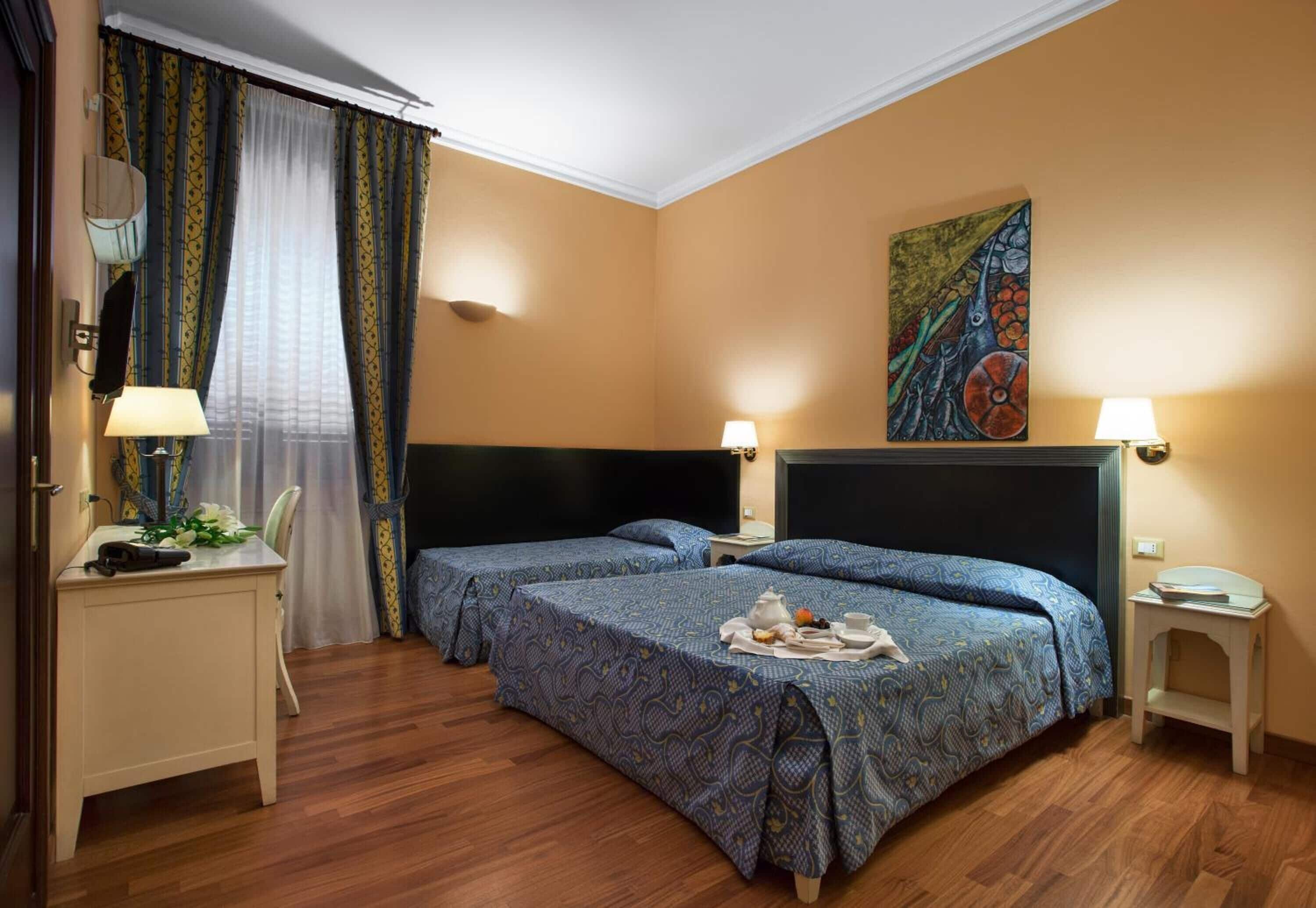 Une chambre d’hôtel avec deux lits, un bureau, une chaise, une télévision et un tableau au mur.