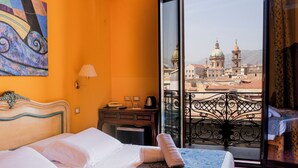 Habitación de hotel con cama, escritorio, lámpara y vista a un paisaje urbano con edificios con cúpulas.