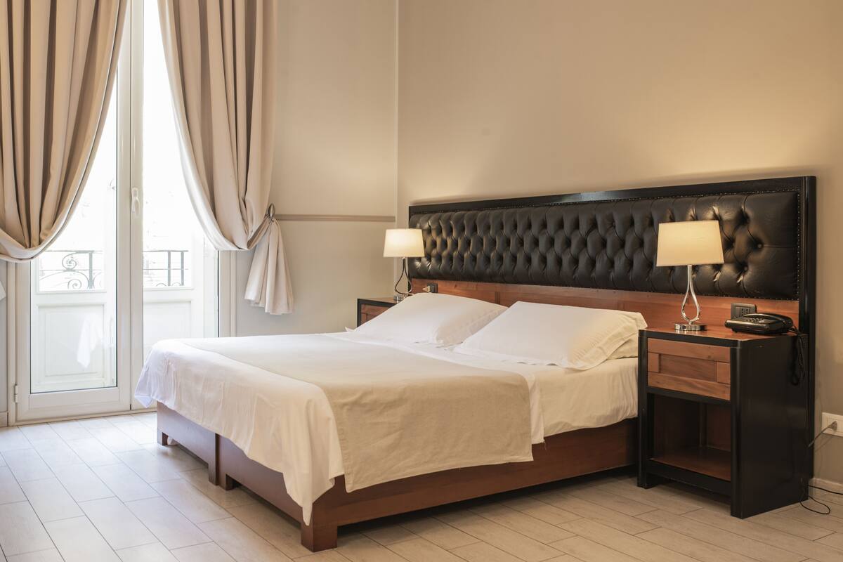 A neatly made bed with white linens, a tufted headboard, bedside lamps, and a wooden nightstand.