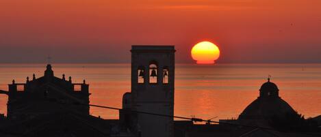 A sunset over a body of water with a bell tower and domed buildings in the foreground.