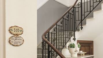 A staircase with a wooden handrail and black metal balusters, a white wall with a door labeled '510', and a wooden cabinet with a plant on top.
