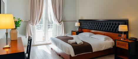 Une chambre d’hôtel avec un grand lit, deux tables de chevet avec des lampes, un bureau avec une lampe et une vue sur l’extérieur par une fenêtre avec des rideaux.