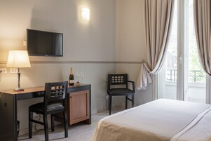A hotel room with a bed, a desk with a chair, a television mounted on the wall, and a window with curtains.