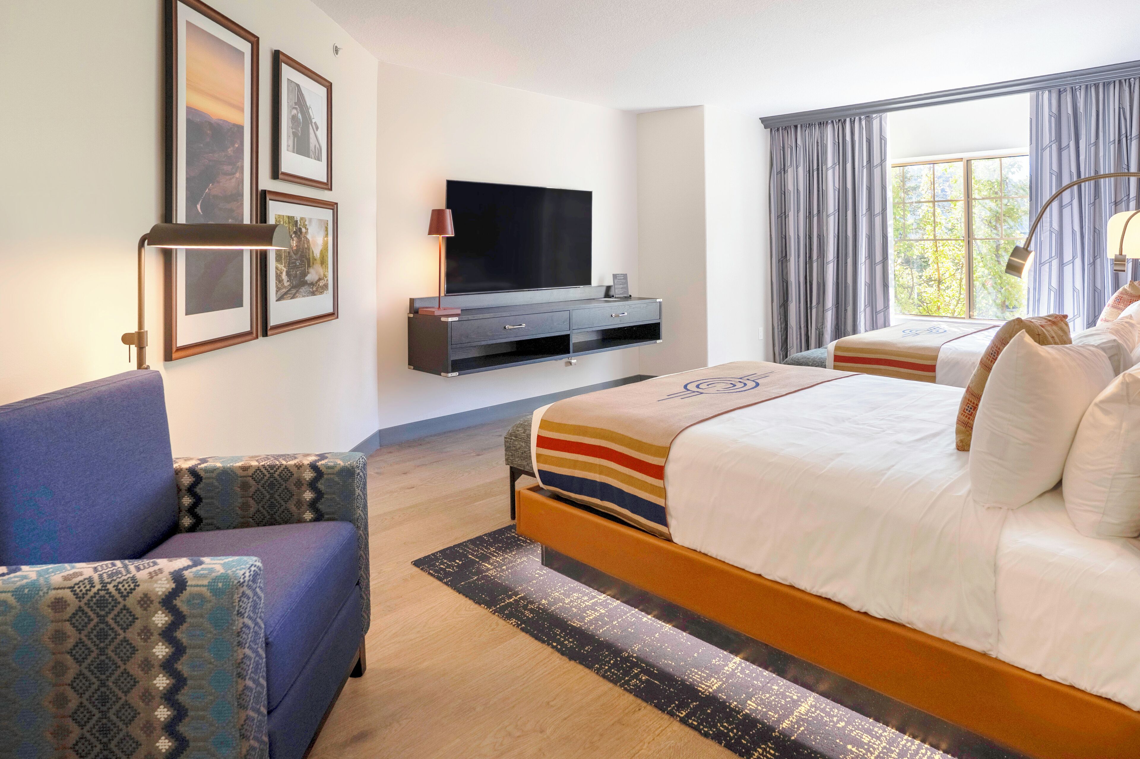 A hotel room with a bed, a TV, a sofa, and a window with curtains.