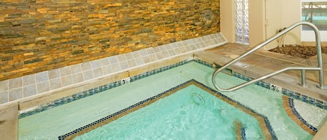 A swimming pool with a stone wall, a tiled floor, and a metal ladder.
