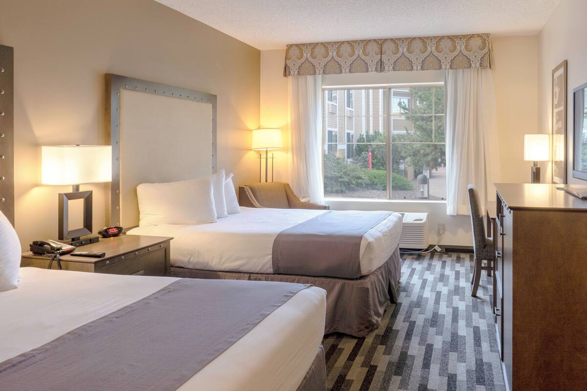 Hotelkamer met twee bedden, een bureau, een stoel, een lamp en een raam met uitzicht.