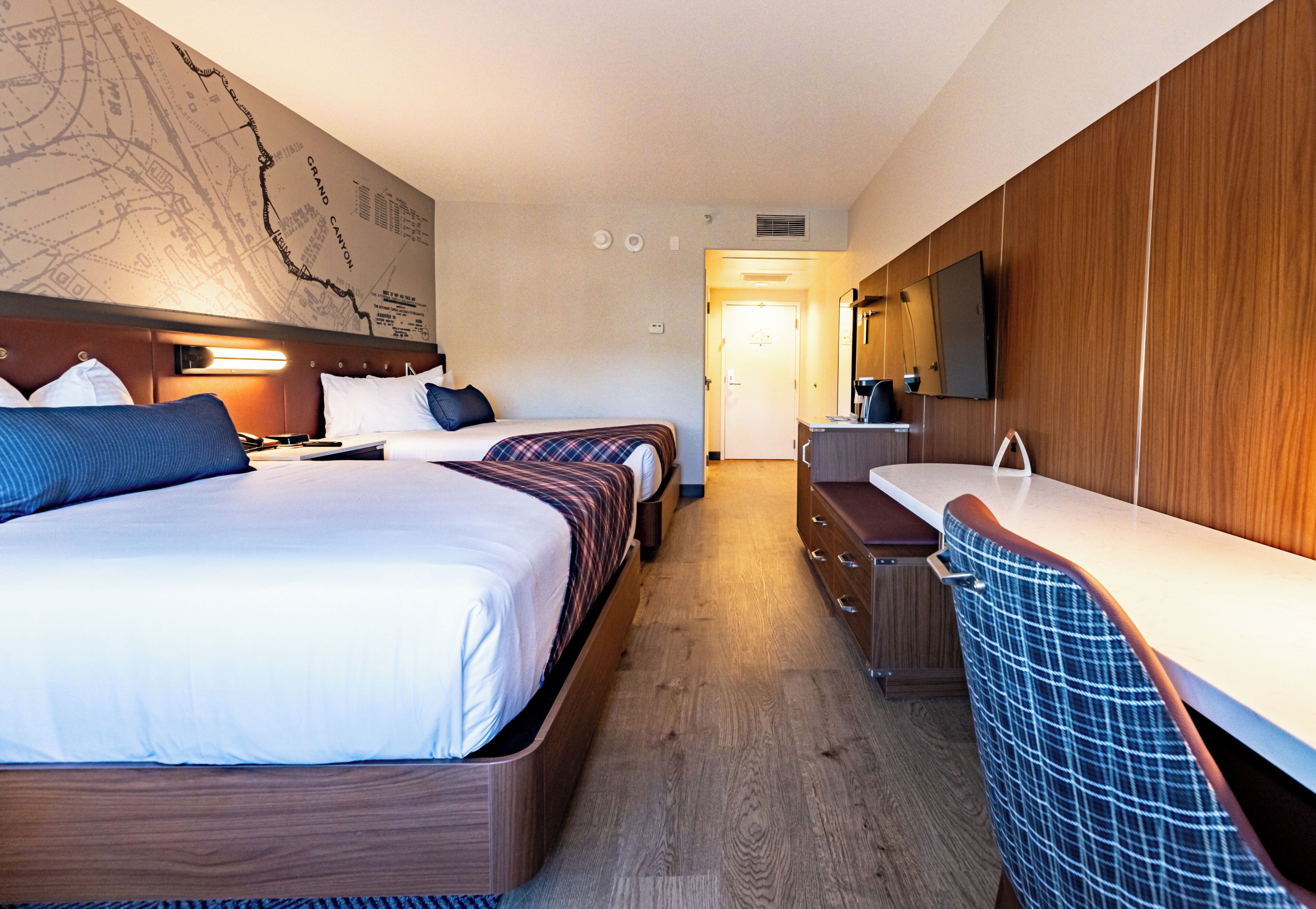 A hotel room with two beds, a large wall map, a wooden vanity, and a mirror.