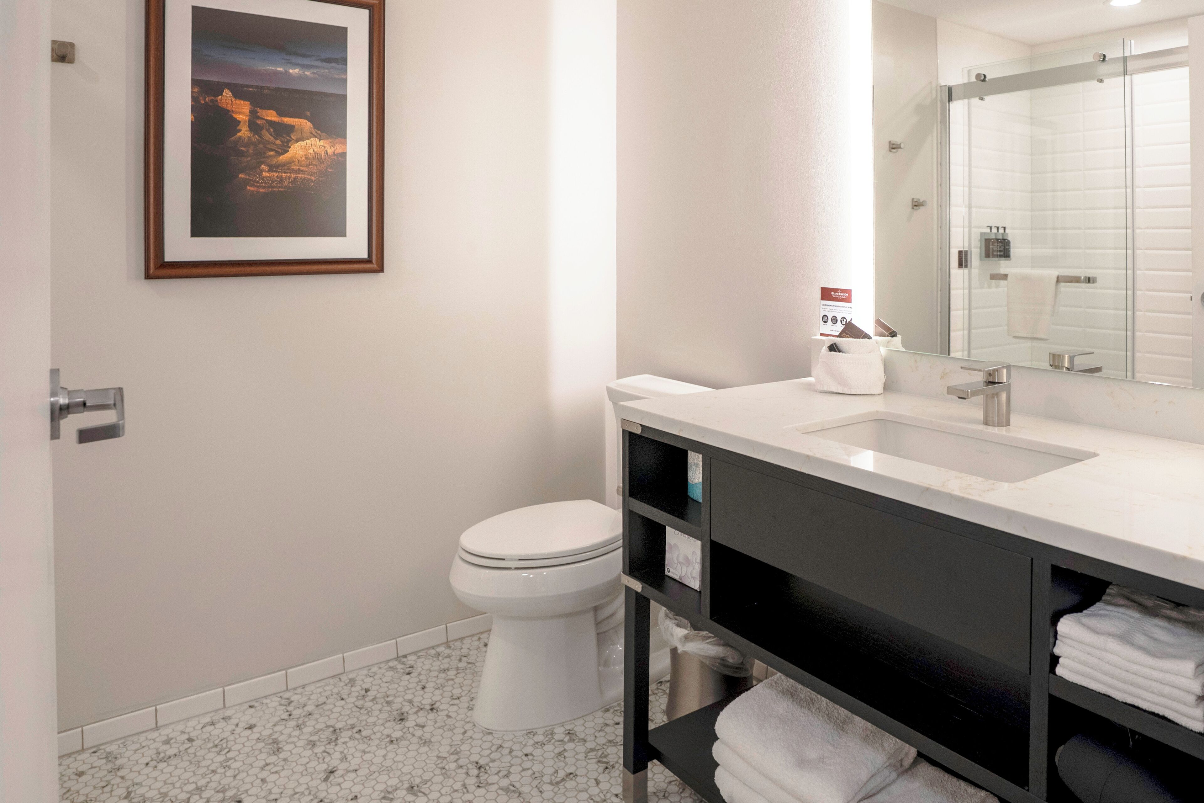 A modern bathroom with a white toilet, a sink with a mirror, and a framed picture on the wall.