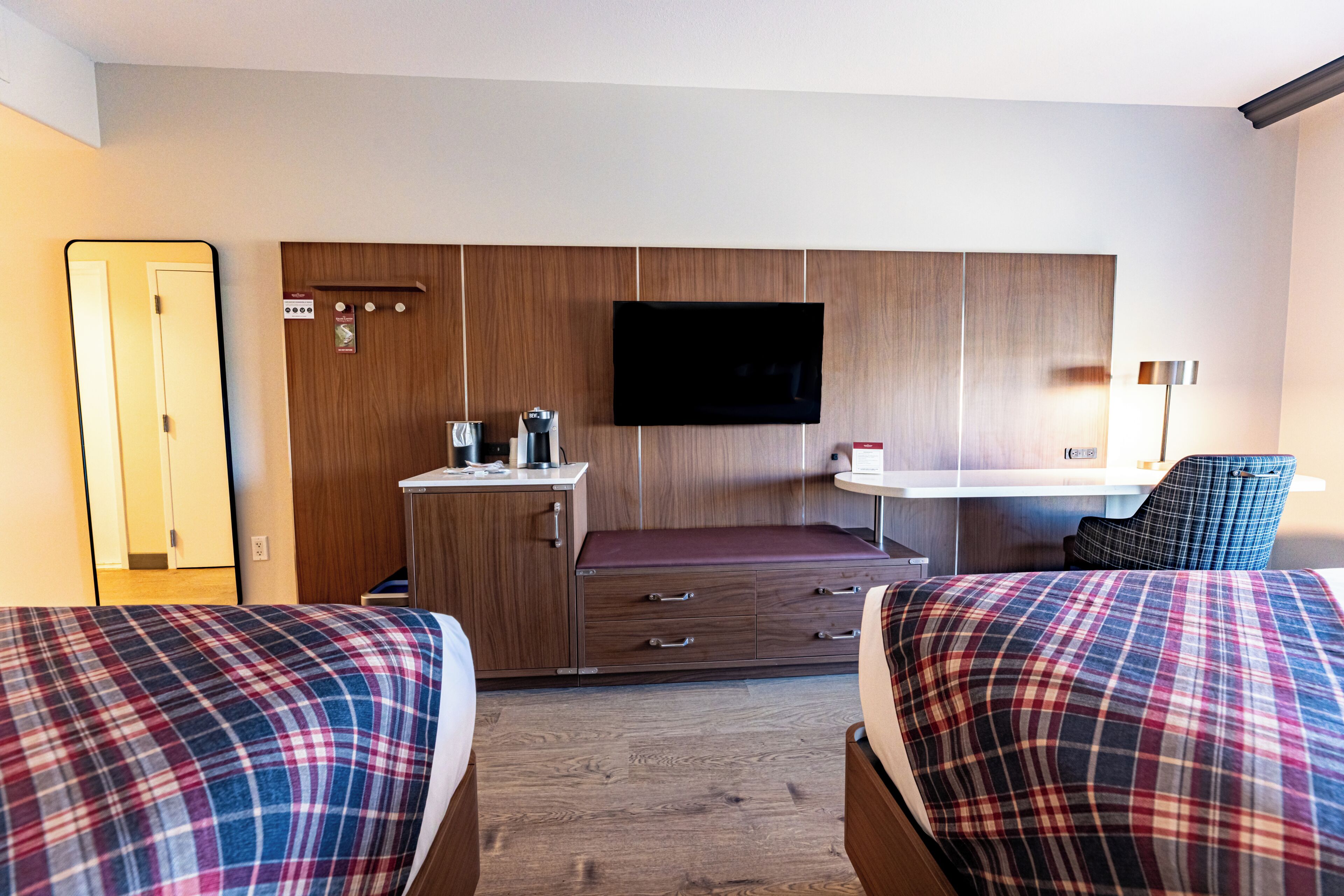 A hotel room with two beds, a desk, a TV, and a chair.
