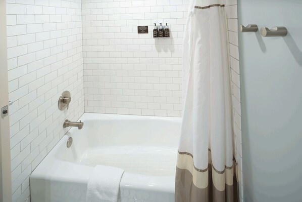 A bathroom with a white tiled wall, a bathtub, a shower curtain, and a towel rack with bottles.