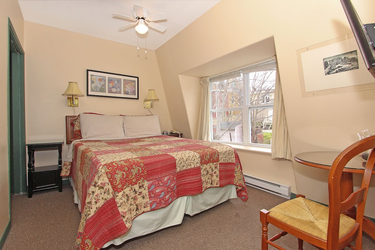Une chambre à coucher comprenant un lit, deux lampes de chevet, un ventilateur de plafond, une fenêtre avec vue et un fauteuil.