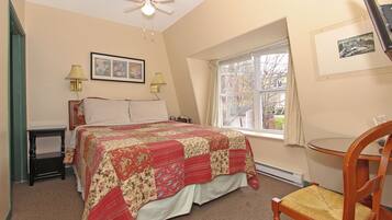 A bedroom with a bed, two bedside lamps, a ceiling fan, a window with a view, and a chair.
