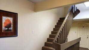A staircase with a wooden handrail leading to a landing, a framed picture on the wall, and a white door at the end. - Gower Guest House (St. John's)