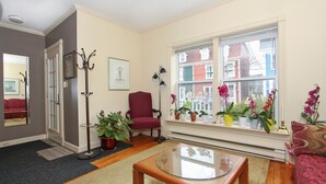 A living room with a glass coffee table, a red armchair, and a large window with potted plants. - Gower Guest House (St. John's)