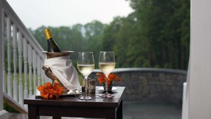 A table with a bottle of champagne, two glasses of white wine, and a vase with orange flowers on a balcony overlooking a stone bridge and greenery. - Kemble Inn (Lenox)