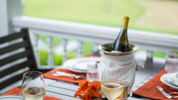 A dining table set with plates, glasses, and a bottle of champagne, with a view of a green landscape.