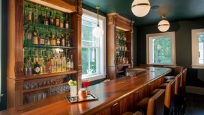 A bar area with wooden bar counters, shelves of liquor bottles, and a long bar stool seating arrangement. - Kemble Inn (Lenox)