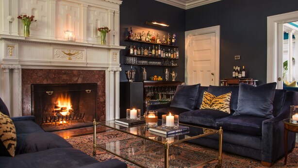 A cozy living room with a fireplace, a dark blue sofa, and a coffee table. - Kemble Inn (Lenox)