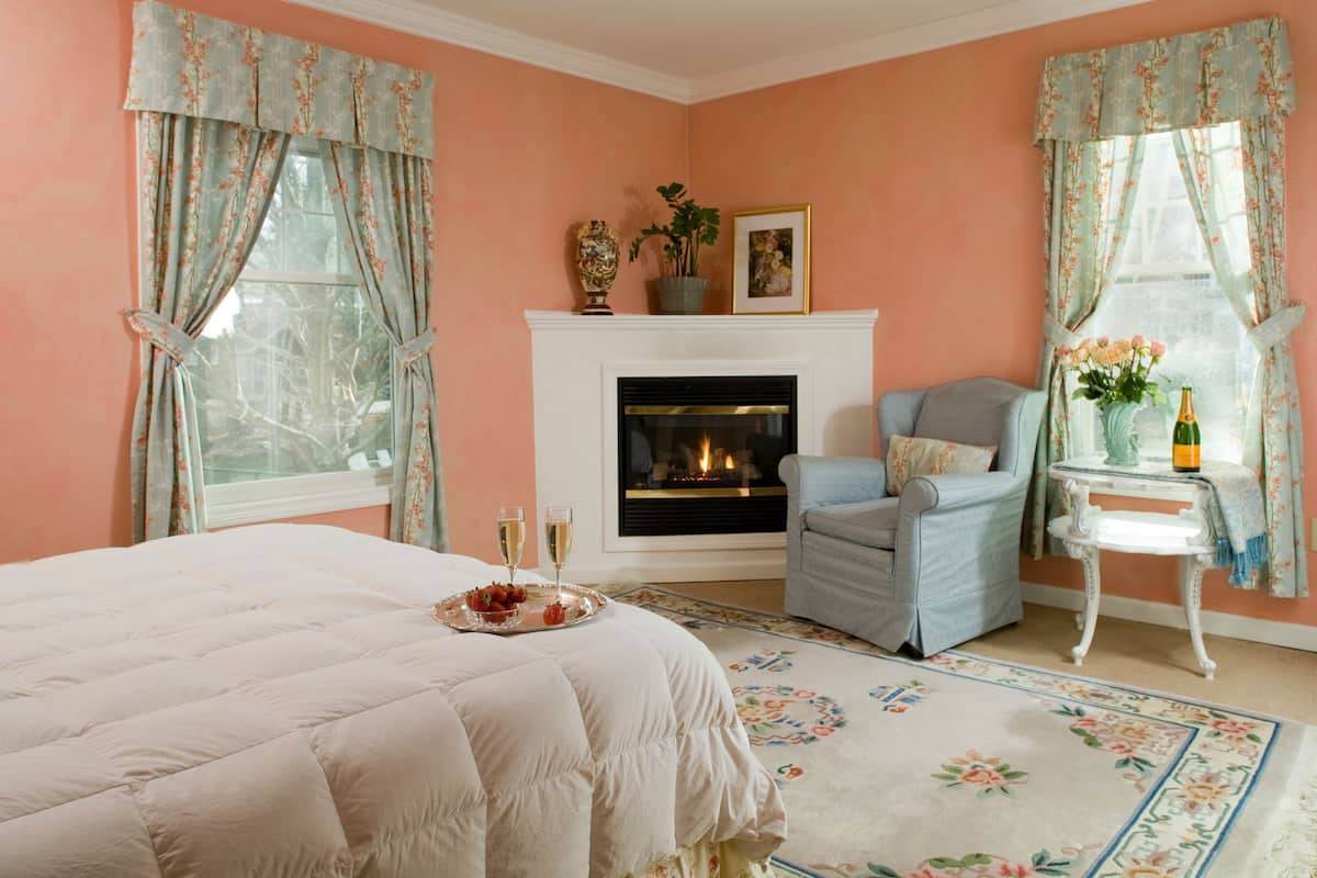 Una camera da letto con un letto, un camino, una sedia e un tavolino con una bottiglia e fiori.