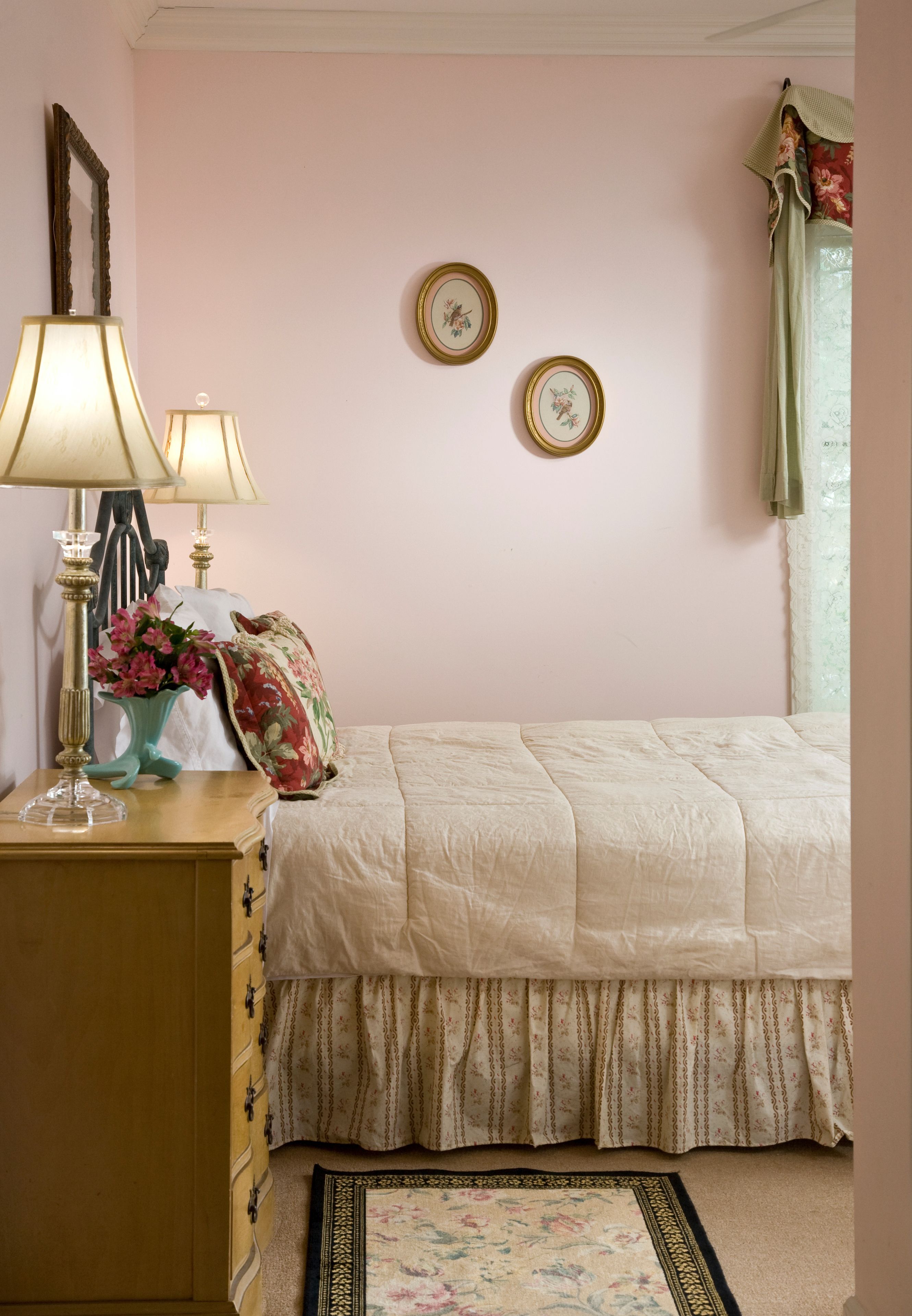 A bedroom with a bed, two bedside lamps, a dresser, a floral rug, and two framed pictures on the wall.