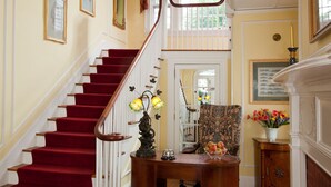 A grand staircase with red carpeted steps and a wooden handrail, leading to a landing with a vase of flowers and a framed picture. - Hampton Terrace Inn (Lenox)