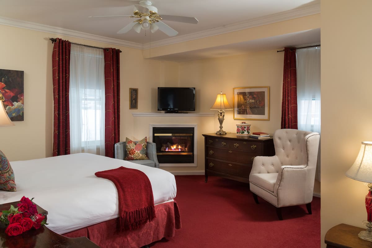 Una camera d'albergo con un letto, un caminetto, una televisione, una poltrona e una lampada.