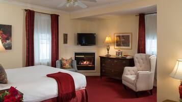 A hotel room with a bed, a fireplace, a television, a chair, and a lamp.