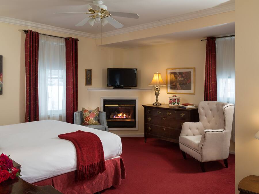 A hotel room with a bed, a fireplace, a television, a chair, and a lamp.