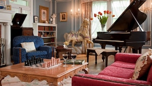 A room with a grand piano, a chessboard, a horse statue, and a blue armchair. - Hampton Terrace Inn (Lenox)