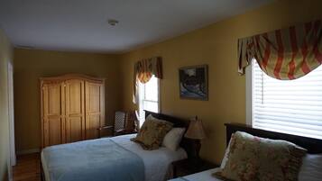 A bedroom with two beds, a wooden wardrobe, a painting on the wall, and a window with curtains.