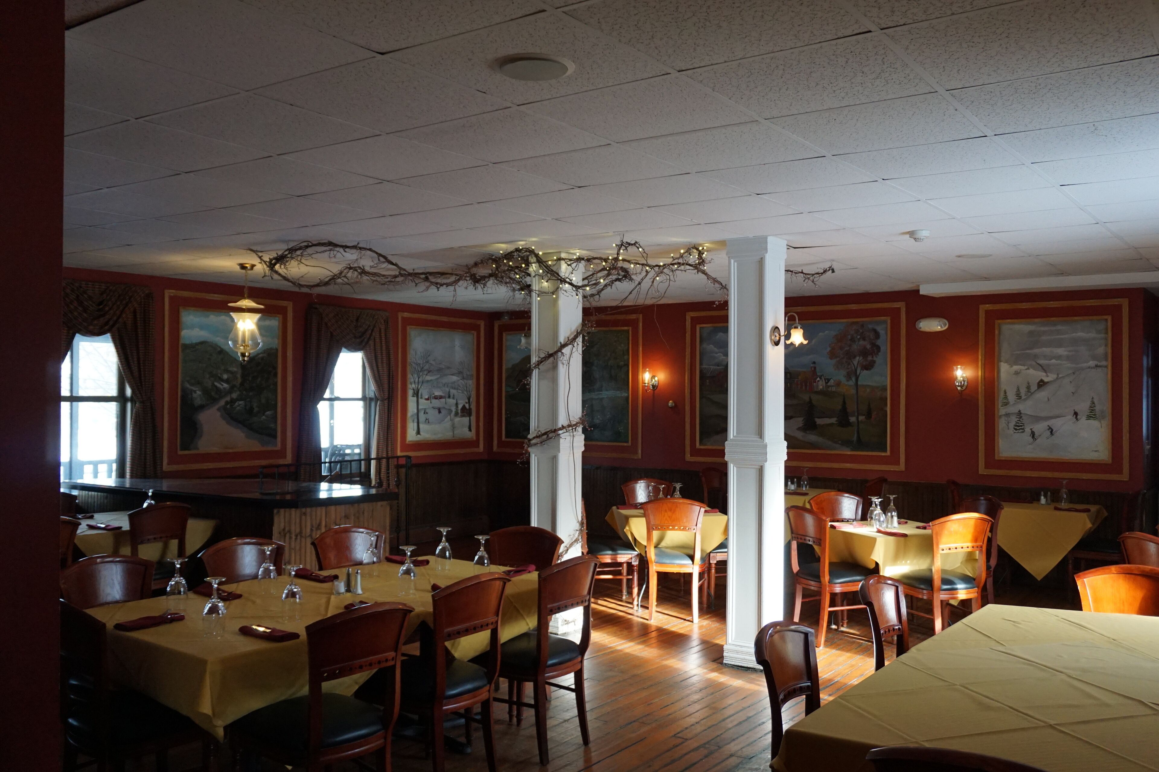 Un restaurant avec des tables et des chaises en bois, des œuvres d’art encadrées accrochées aux murs et un lustre.