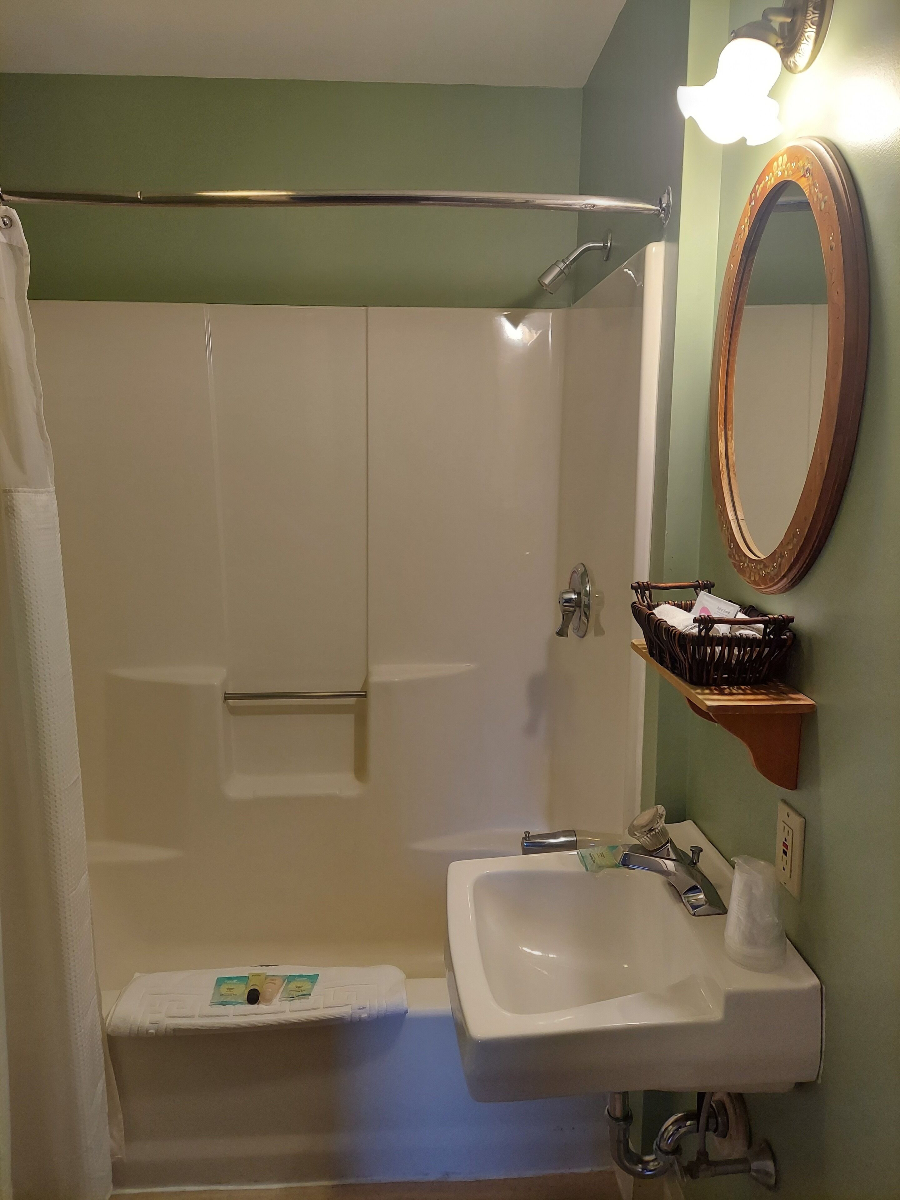 Een badkamer met een douche, wastafel, spiegel en een plank met toiletartikelen.