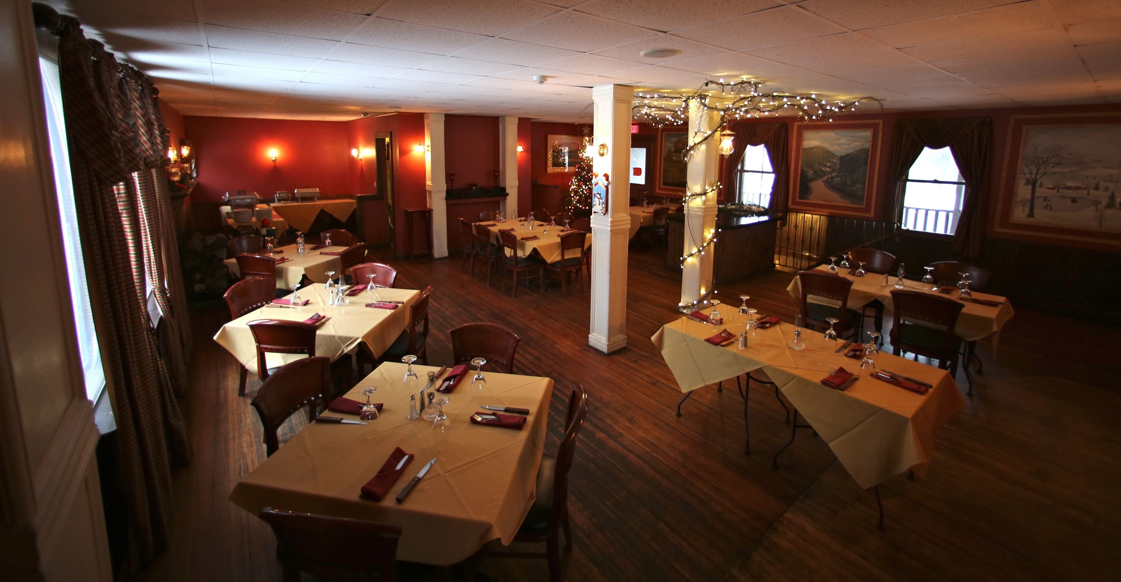 Un restaurant avec plusieurs tables dressées pour le dîner, un plancher en bois et un sapin de Noël en arrière-plan.