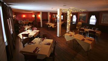 Un restaurant avec plusieurs tables dressées pour le dîner, un plancher en bois et un sapin de Noël en arrière-plan.