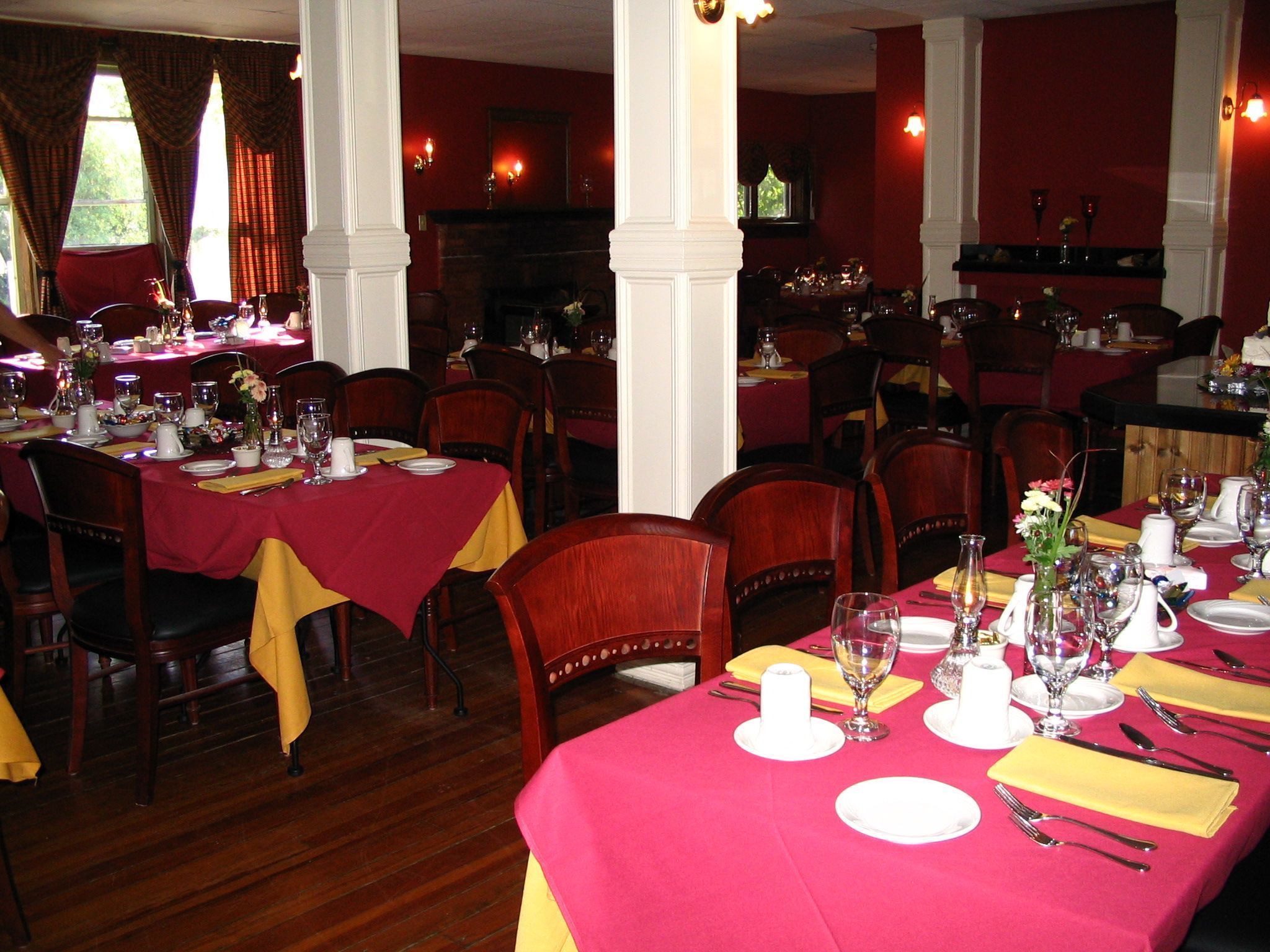 A dining area with tables set for multiple guests, featuring red and yellow tablecloths, white plates, and glassware.