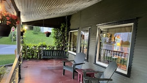 Eine überdachte Veranda mit zwei Adirondack-Stühlen, einem kleinen Tisch und hängenden Blumenkörben.