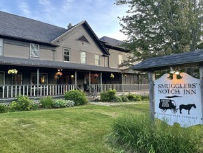 A two-story building with a porch, a sign for 'Smugglers' Notch Inn', and a logo for 'Lodging, Food Spirits Bakery'.
