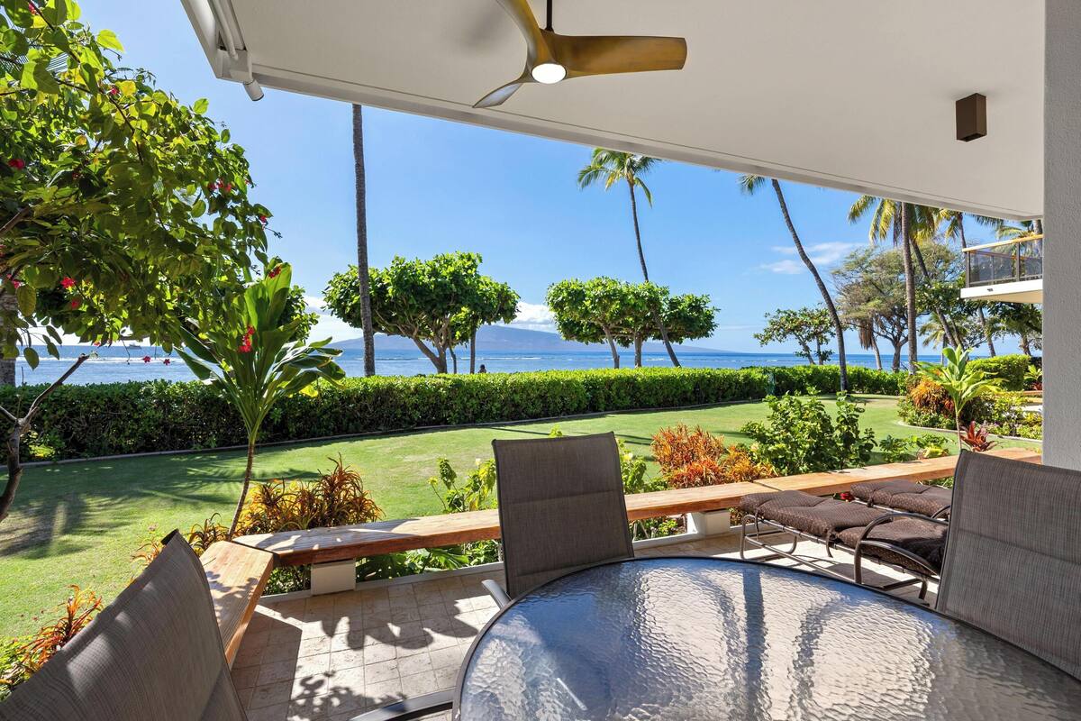 A covered outdoor seating area with a view of the ocean and a clear sky.