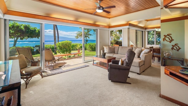 A spacious living area with a large sliding glass door leading to a balcony with a view of the ocean. There is a ceiling fan, a sofa, and a coffee table. - Puunoa  - CoralTree Residence Collection (Lahaina)