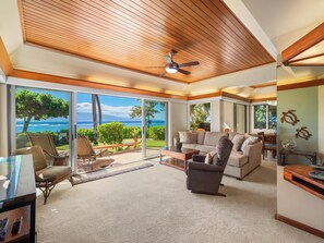 A spacious living area with a large sliding glass door leading to a balcony with a view of the ocean. There is a ceiling fan, a sofa, and a coffee table. - Puunoa  - CoralTree Residence Collection (Lahaina)