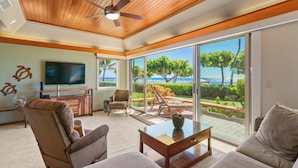 A modern living room with a ceiling fan, a flat-screen TV, and a view of the ocean through large sliding glass doors. - Puunoa  - CoralTree Residence Collection (Lahaina)
