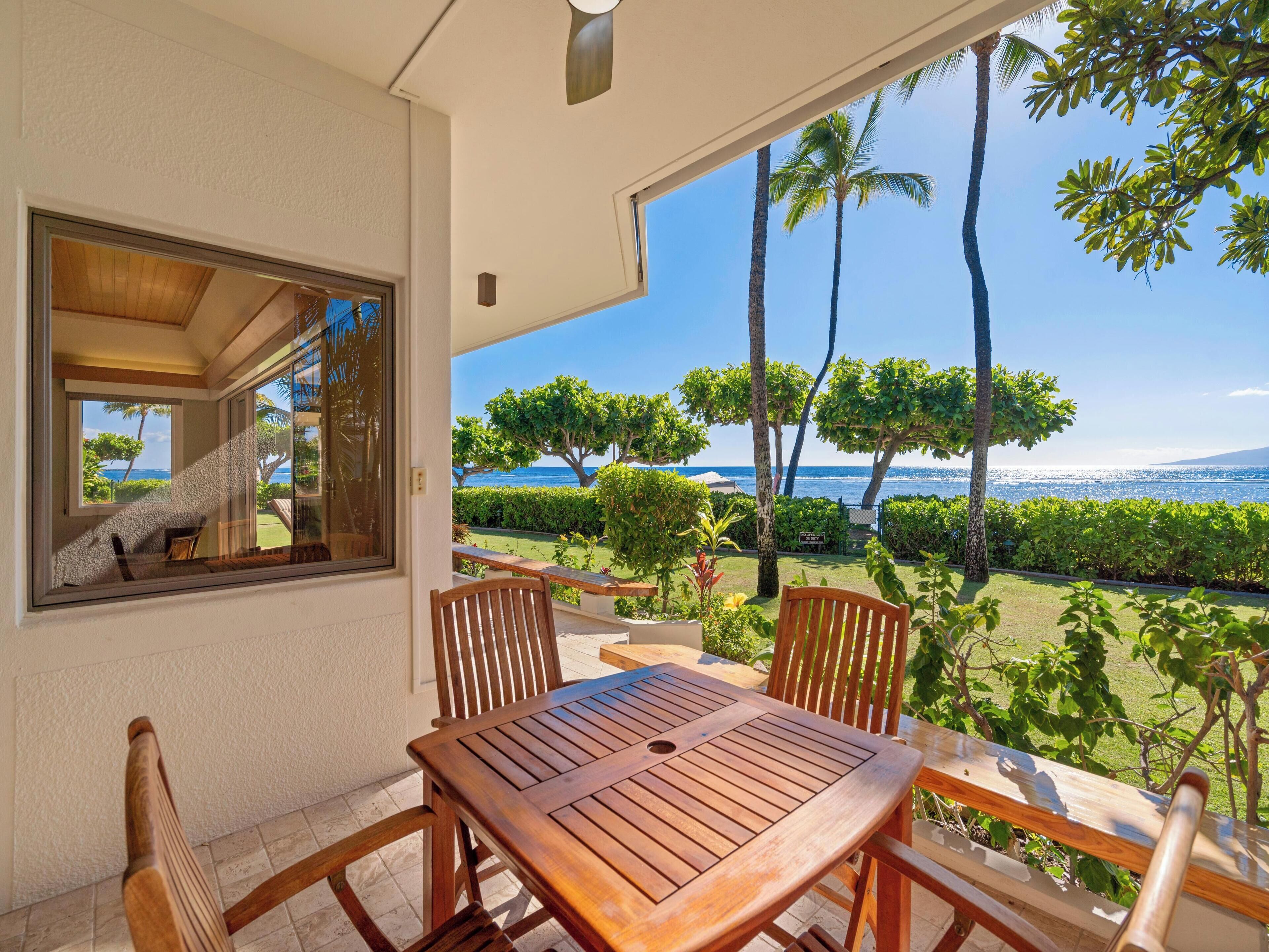 Un tavolo e sedie di legno su un balcone con vista sull'oceano e palme.
