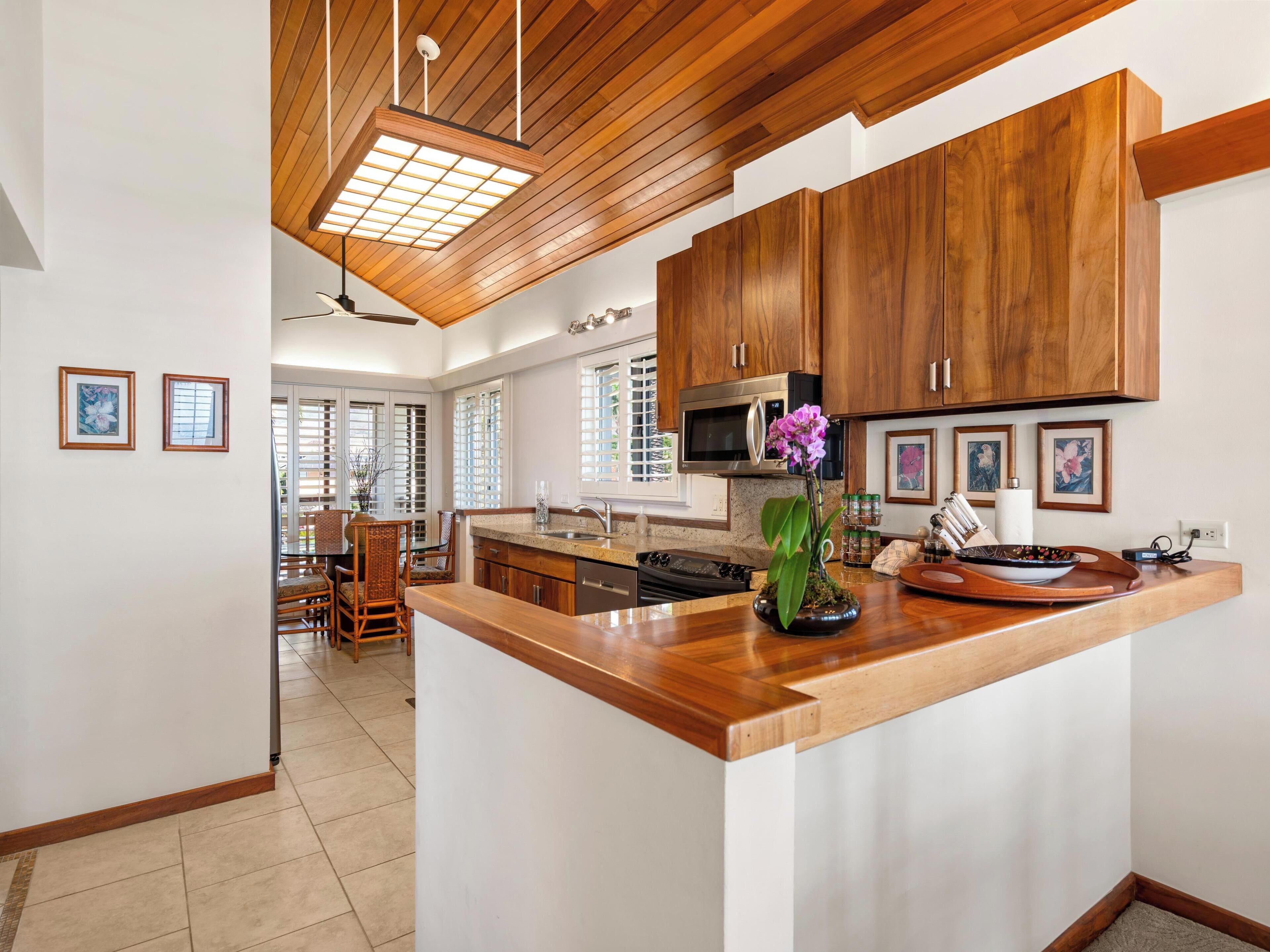 A modern kitchen with wooden cabinets, a central island, and a dining area with chairs.