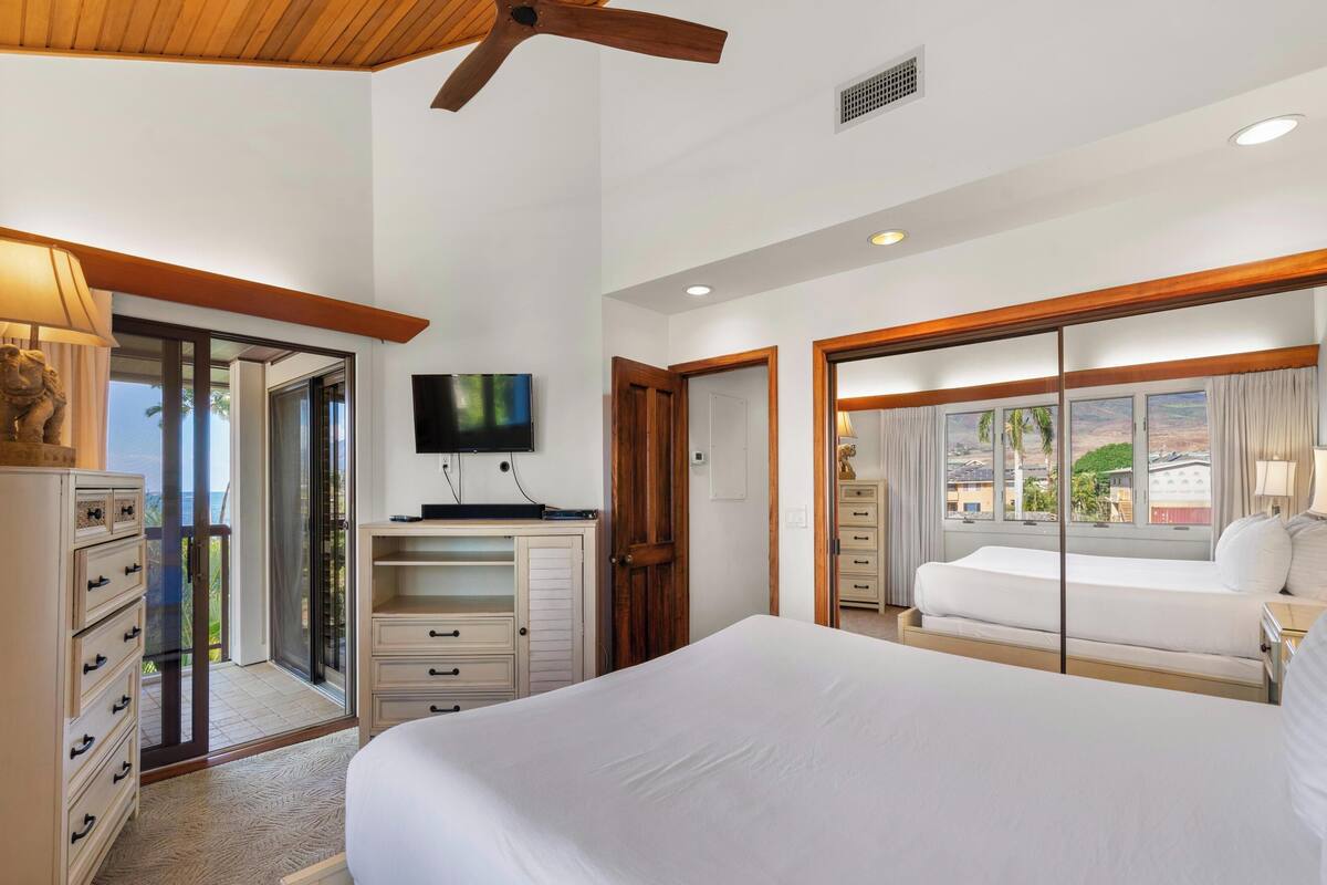 A hotel room with a large bed, a television, a desk, and a view of the outside.