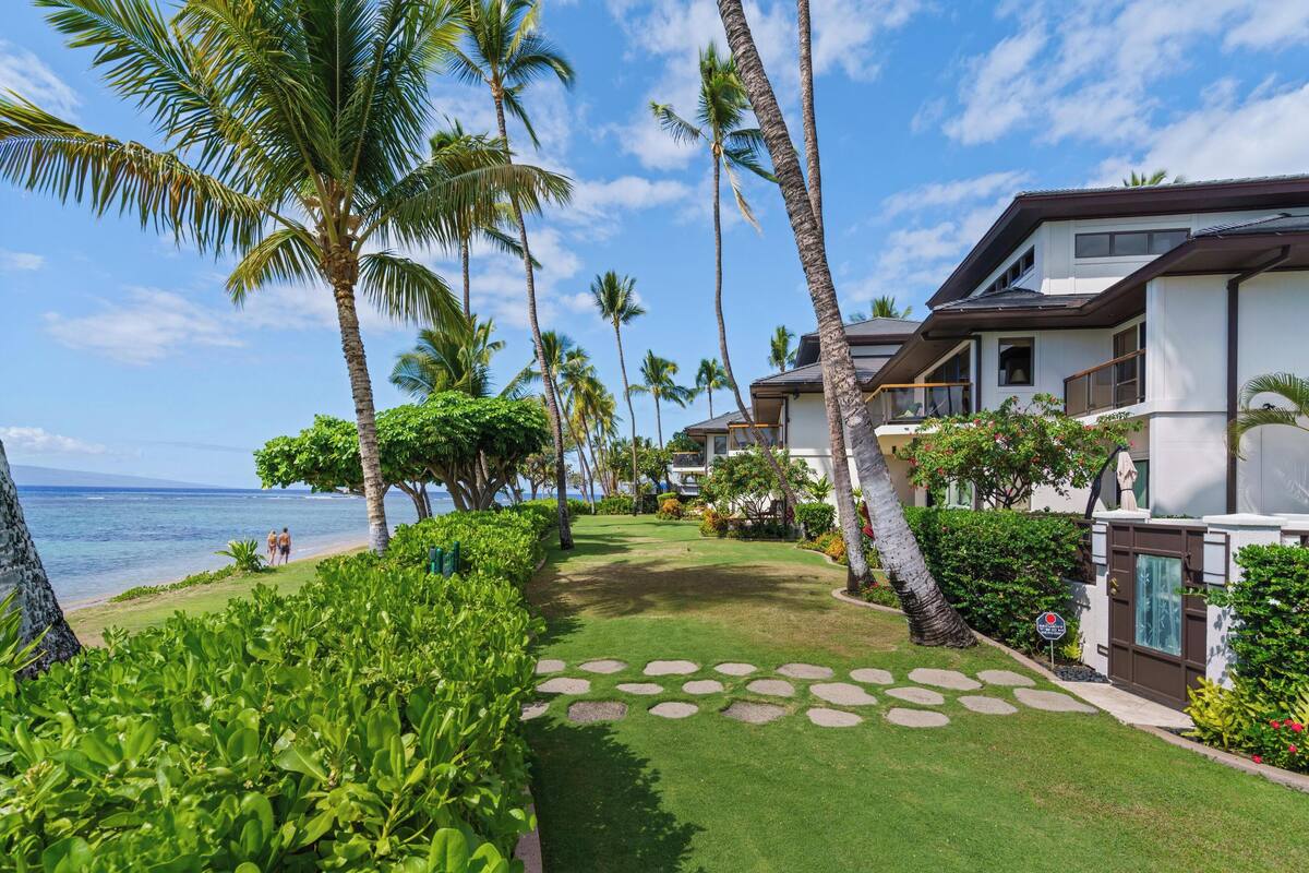 A resort with a well-maintained lawn, palm trees, and a view of the ocean.