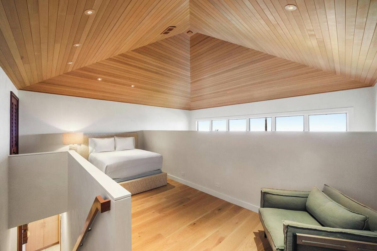 A modern loft bedroom with a sloped ceiling, a bed, a green sofa, and large windows.