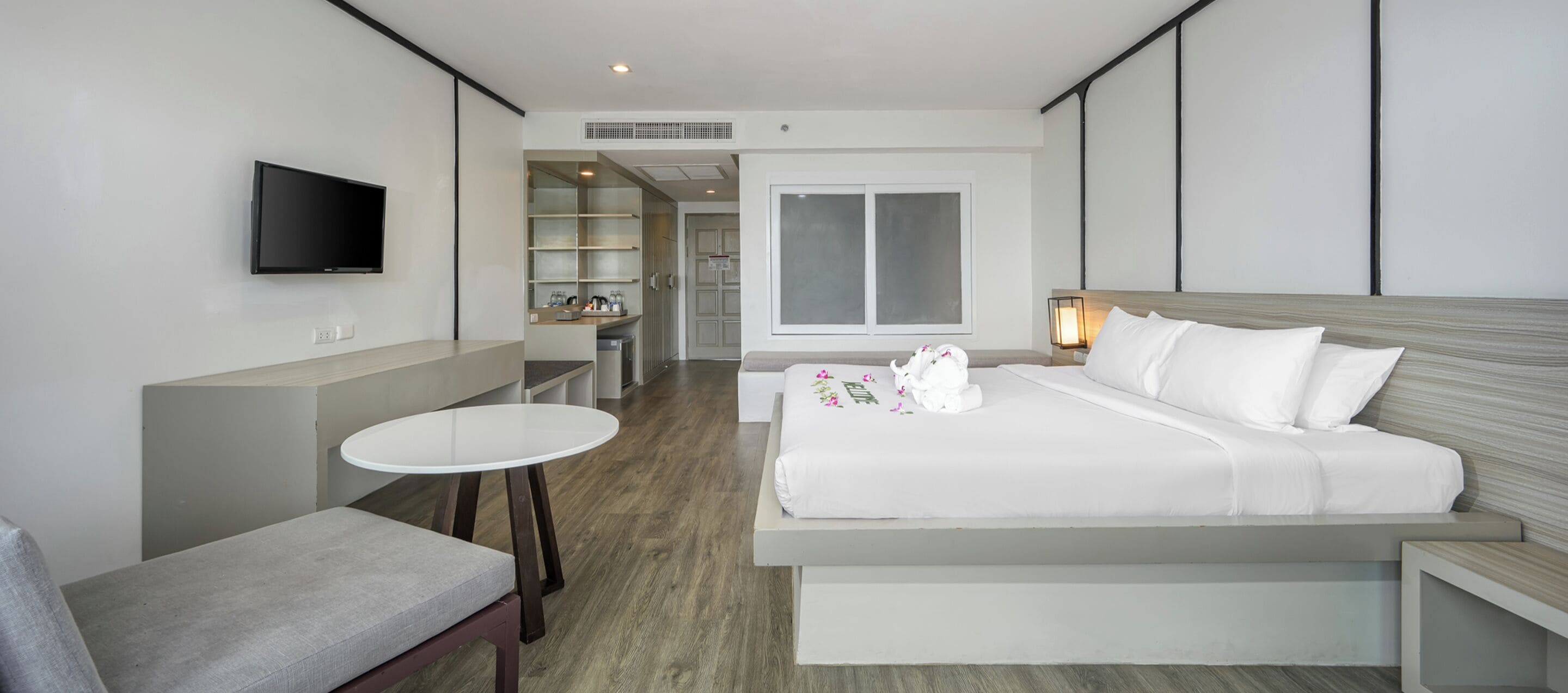 Una camera d'albergo moderna con un letto grande, un tavolino piccolo, una TV a muro e un'area salotto separata con una panca.