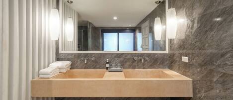 A modern bathroom with a large sink, marble walls, and a glass shower enclosure.
