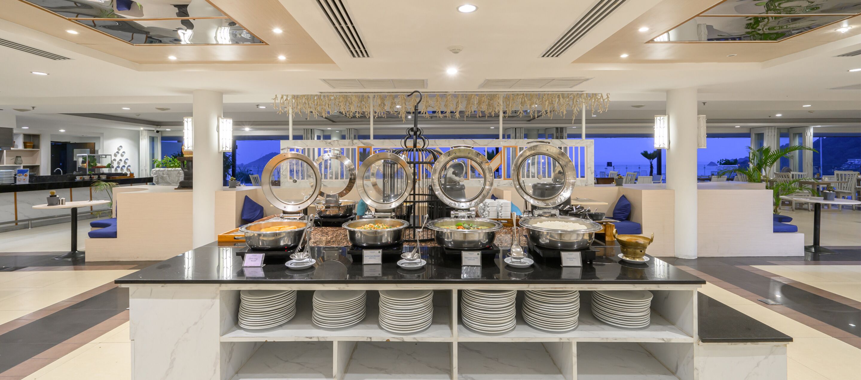 A buffet setup with multiple food stations and a view of the sea in the background.